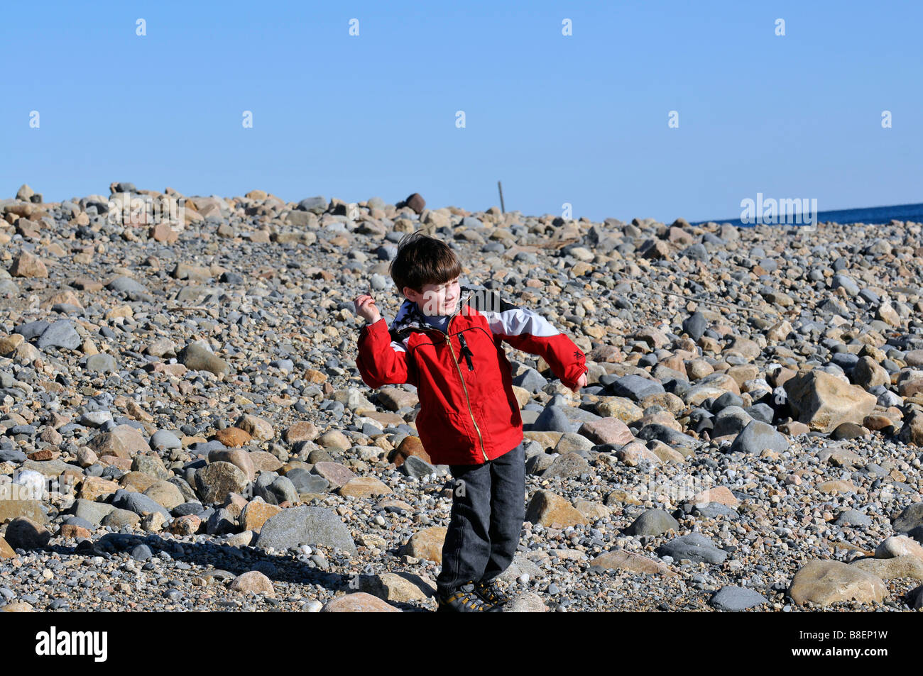 Jeune garçon sur un rivage rocailleux de lancer des pierres dans l'eau au point Judith Phare. Banque D'Images