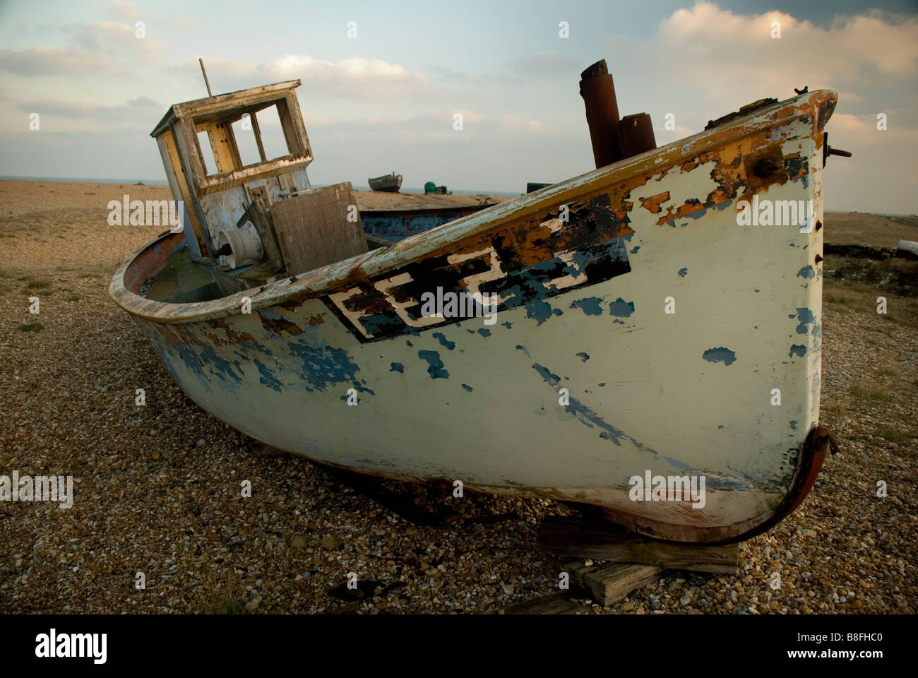 Vieux bateau de pêche en décomposition sur des cailloux à Dungeness, Kent en fin d'après-midi, soleil d'hiver Banque D'Images