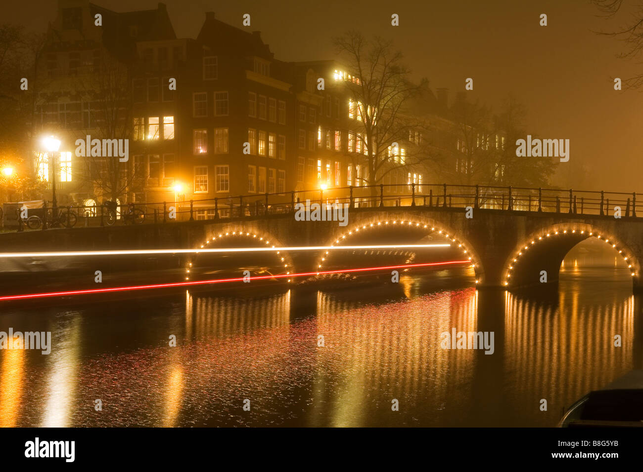 Bateau d'excursion voyages sous un pont lumineux reflète dans canal sur une nuit brumeuse à Amsterdam aux Pays-Bas Banque D'Images