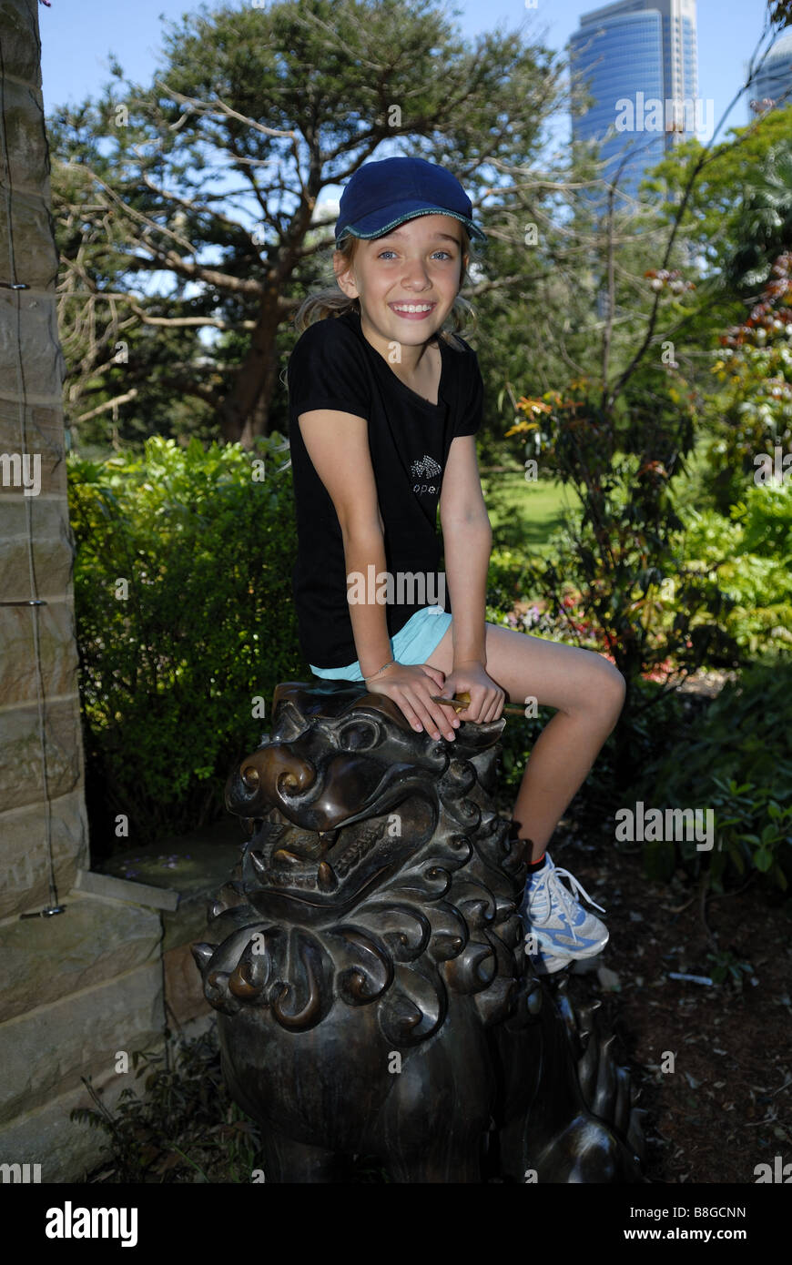 Enfant (10 ans) assis sur l'un des deux lions en bronze, connu sous le nom de Temple des chiens, dans le Royal Botanic Gardens. Sydney, Australie Banque D'Images