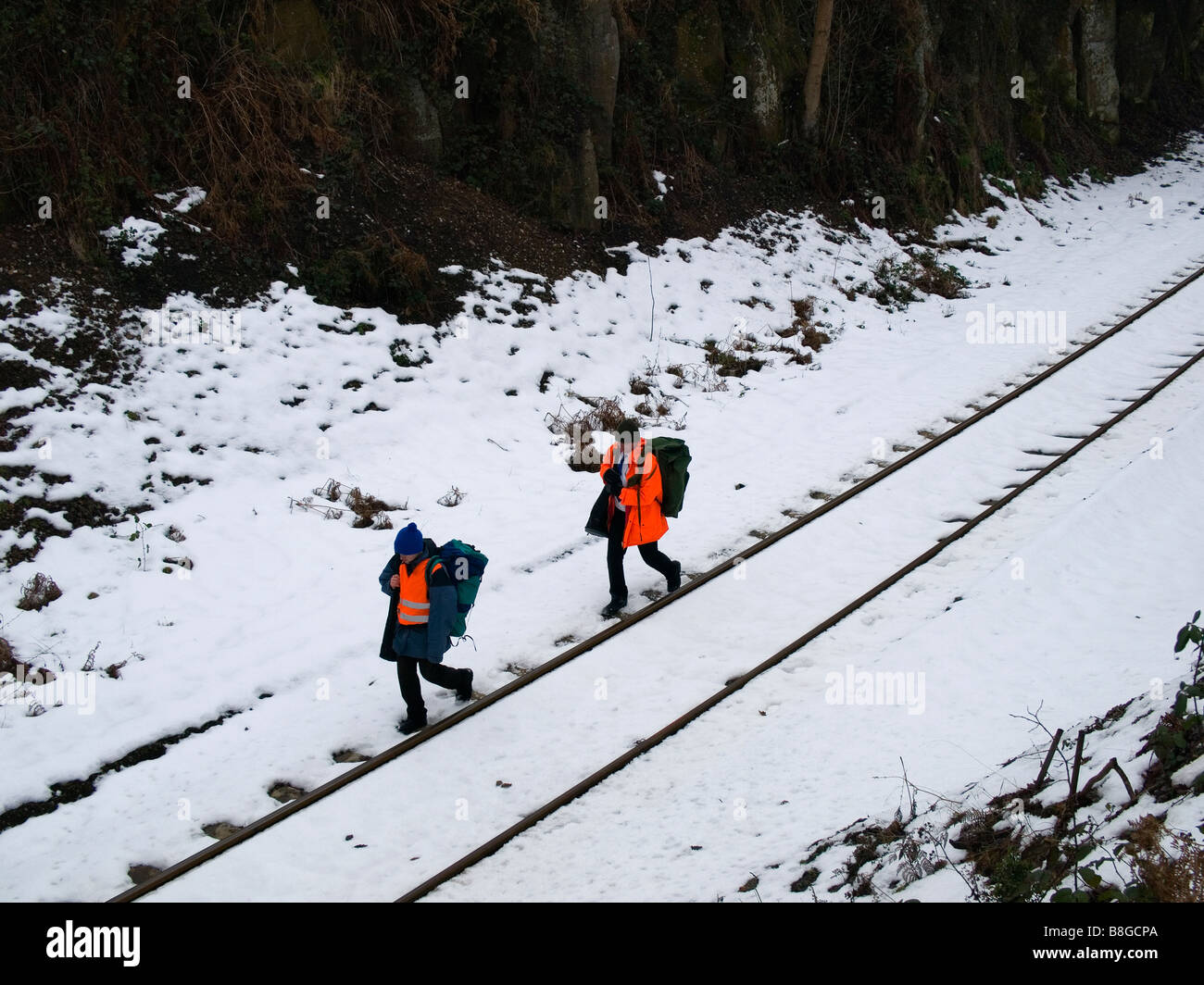 Deux hommes en vestes haute visibilité orange marche sur une ligne de chemin de fer en milieu rural dans la neige Banque D'Images