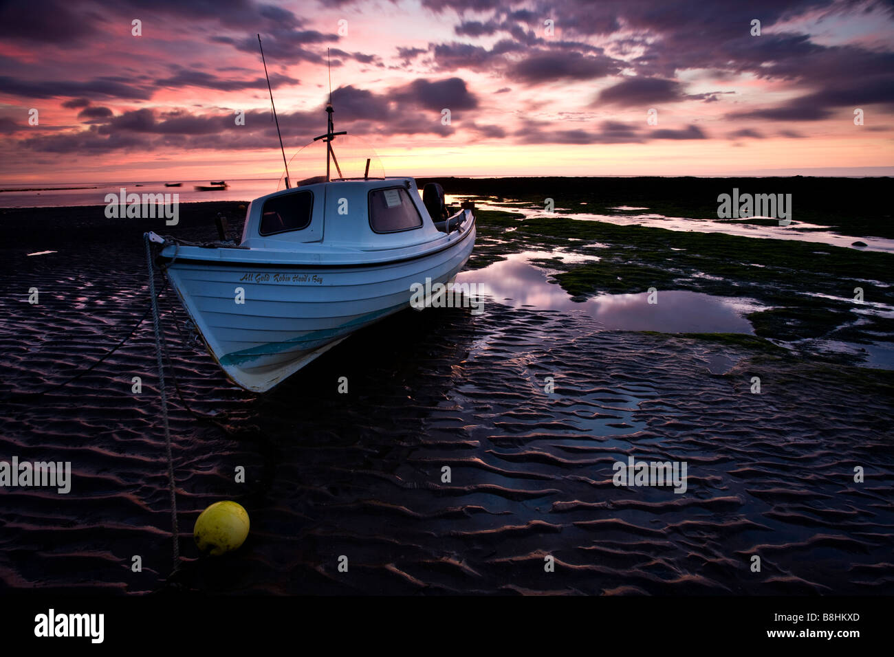 Un petit bateau de pêche sur la plage de Robin Hoods Bay à marée basse avec un beau ciel aube Banque D'Images