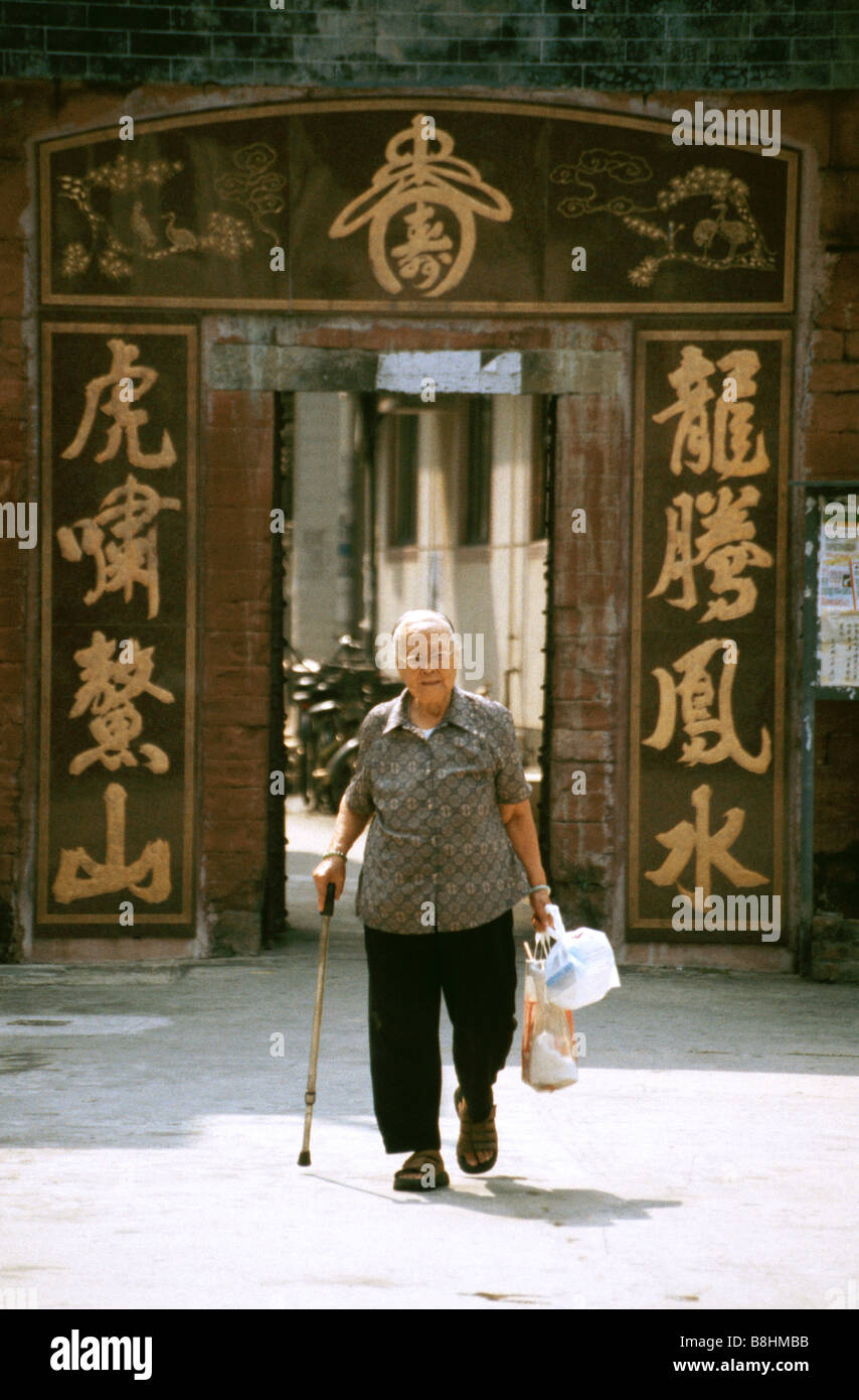 Personnes âgées femme chinoise promenades par l'entrée fermée à la vieille ville de Sheung Shui dans les Nouveaux Territoires, Hong King Banque D'Images