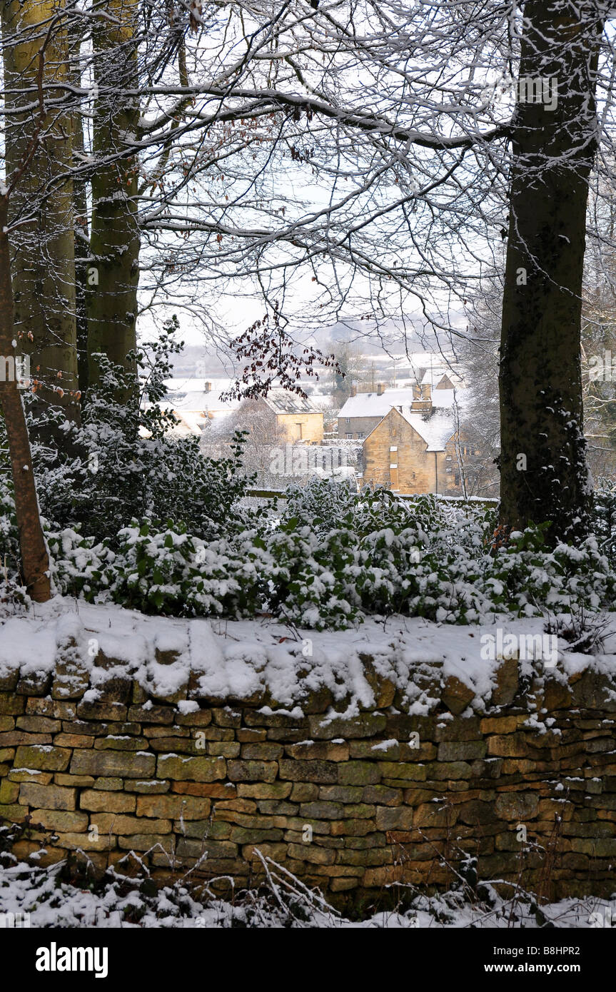 Cottages en pierre de Cotswold vue à travers les arbres dans la neige Banque D'Images