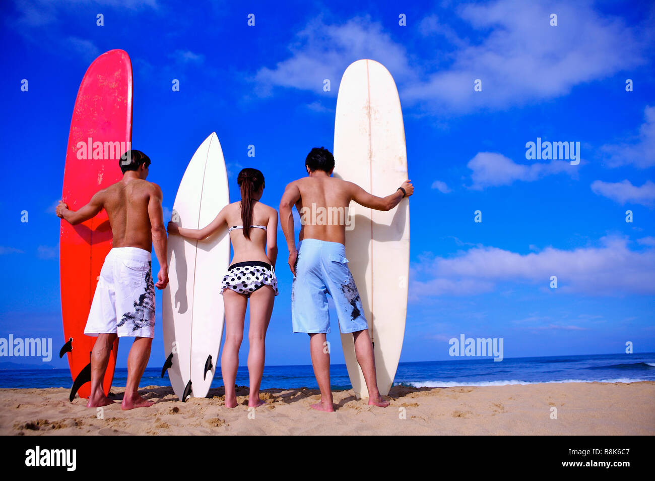 Trois personnes détenant les planches et debout sur la plage vue arrière Banque D'Images