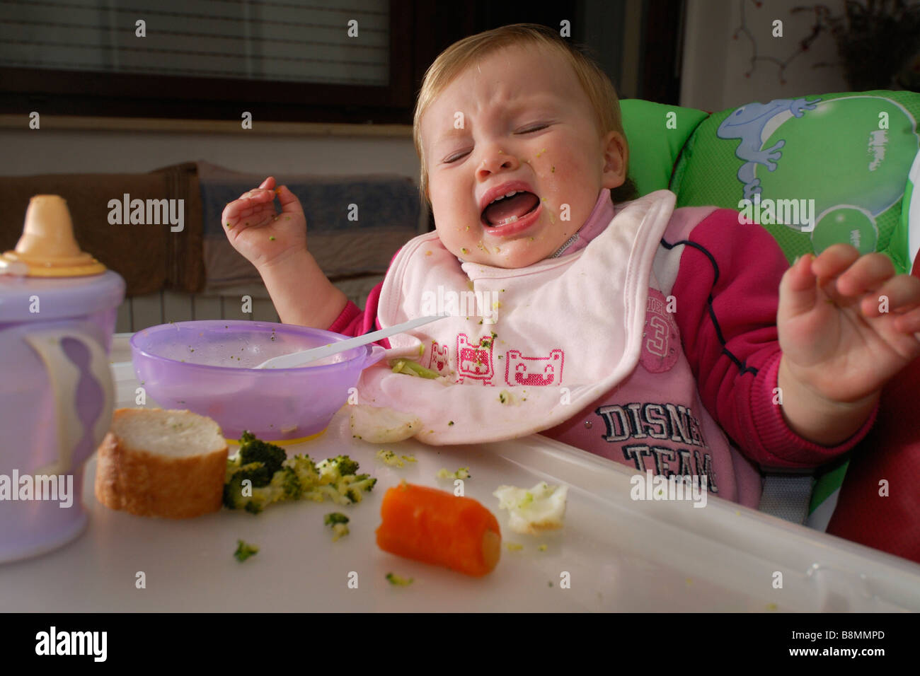 Un an bébé fille pleurer dans une chaise haute à l'heure des repas Banque D'Images