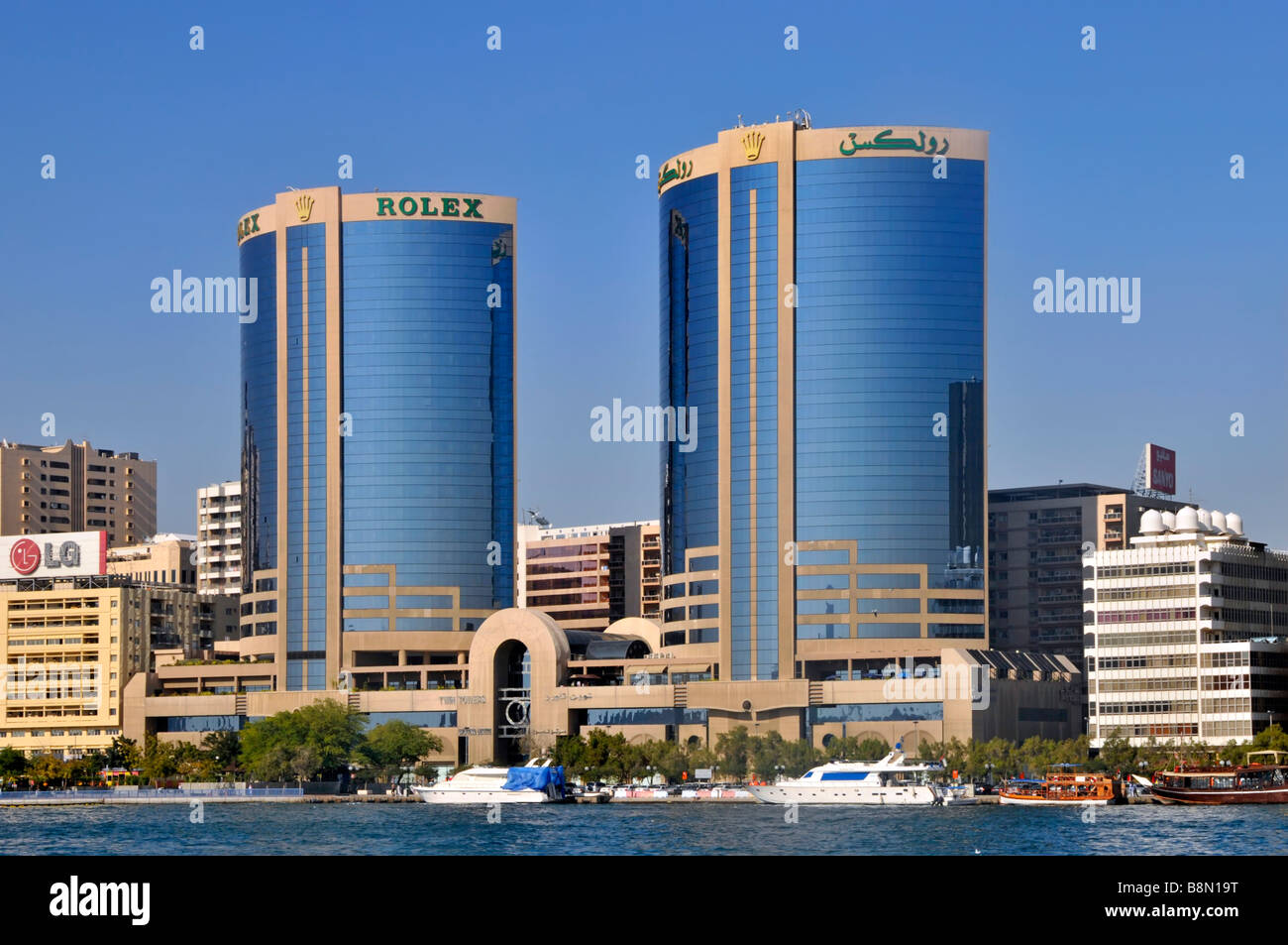 Dubaï deux tours jumelles avec gratte-ciel sur Dubai Creek riverside Skyline un bâtiment avec Rolex publicité Emirats Arabes Unis Eau Asie Banque D'Images