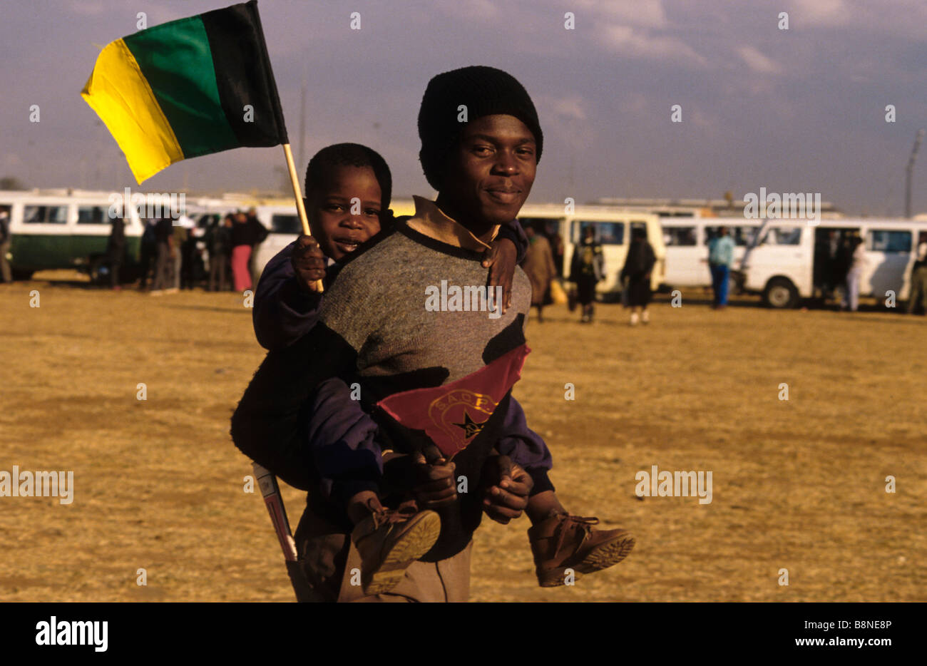 Un homme porte un enfant sur son dos en agitant le drapeau de l'ANC au Soweto lancement d'S.A.C.P (Parti communiste sud-africain) Banque D'Images