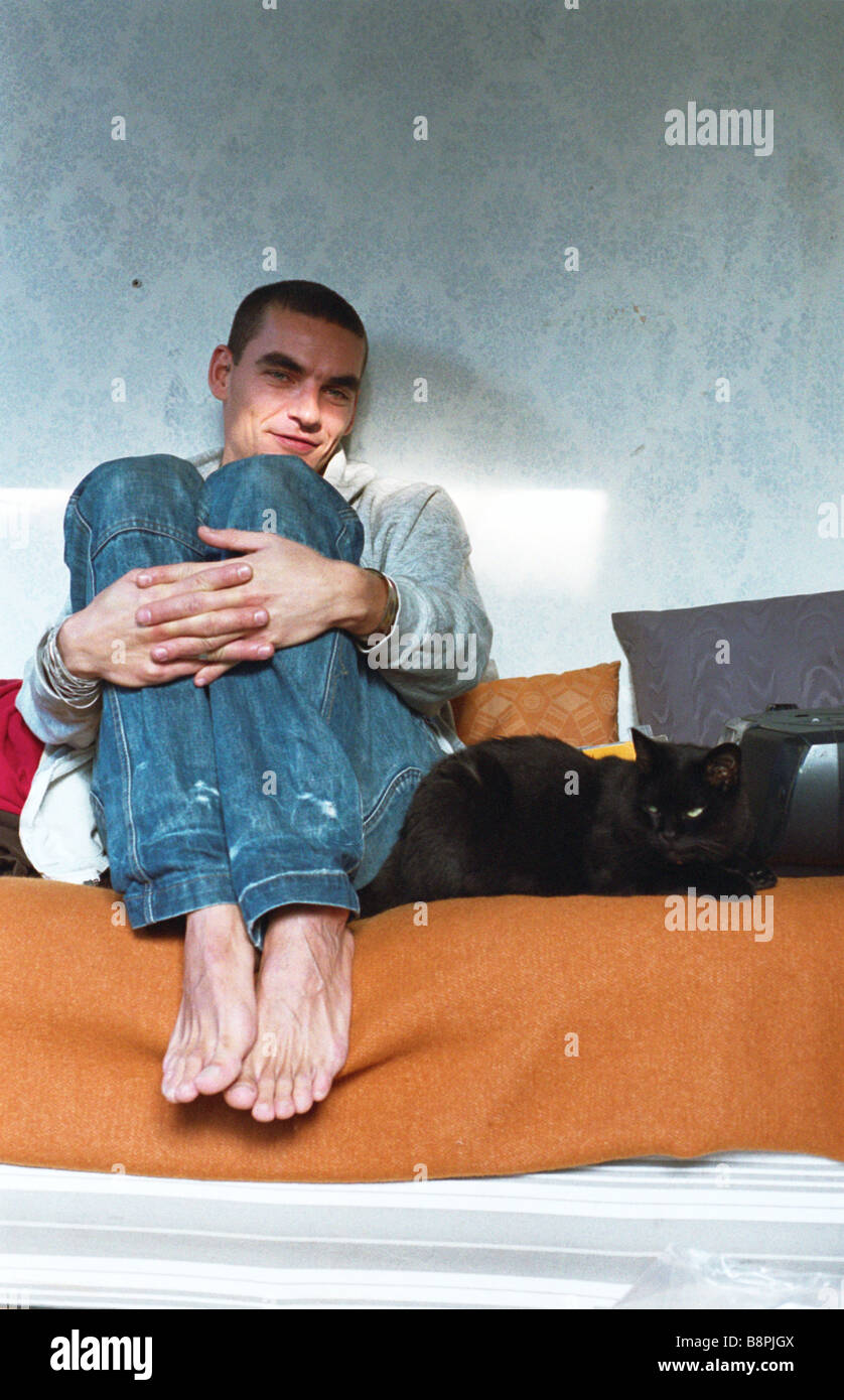 Jeune homme assis au lit, serrant les genoux, le chat couché à côté Banque D'Images