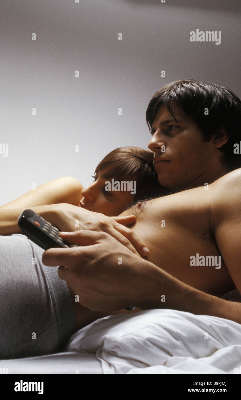 Jeune couple lying together in bed watching television Banque D'Images