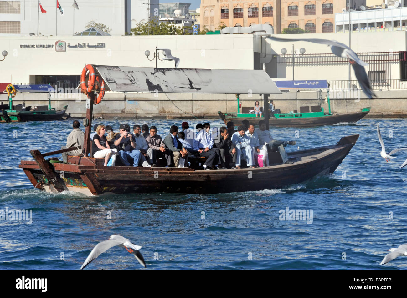Transport à Dubai Creek près du bateau-taxi d'Abras de plus, la foule de passagers comprend des mouettes et une bibliothèque publique au bord de la rivière au-delà des émirats arabes unis Banque D'Images