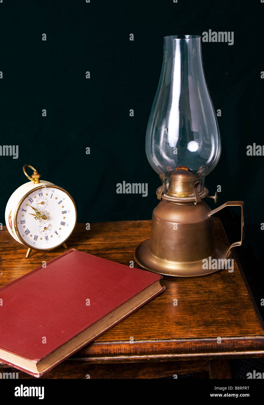Un livre lampe à kérosène et réveil sur une table de chevet Banque D'Images