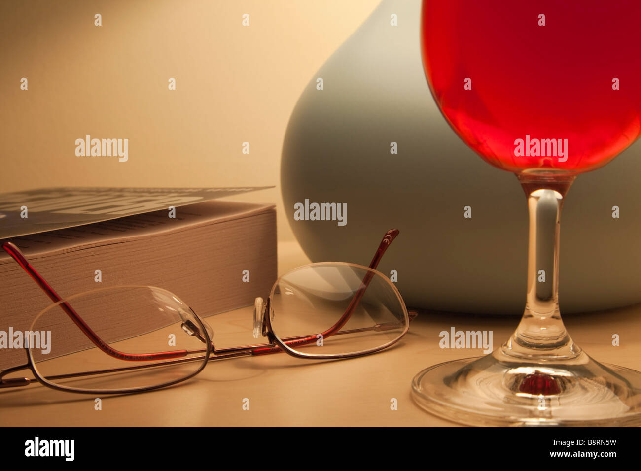 Accueillant tous les jours hygge scène avec un verre de vin rouge par allumé la lampe de chevet Livre de poche et lunettes de lecture à l'heure du coucher. Angleterre Royaume-uni Grande-Bretagne Banque D'Images