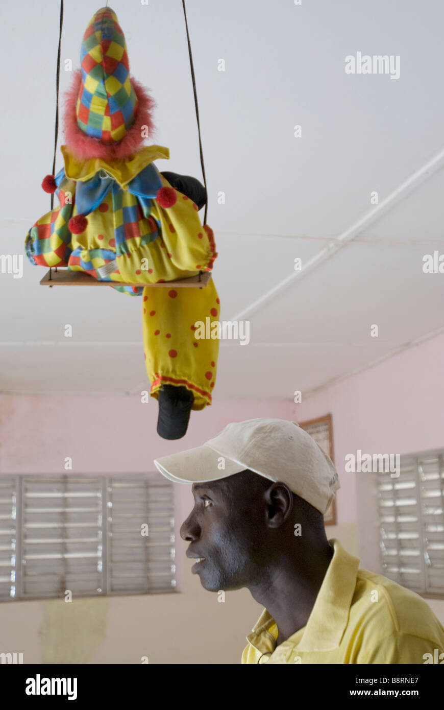 Profil d'un homme médecine africaine avec un enfant sur une balançoire clown jouet au-dessus de sa tête Banque D'Images