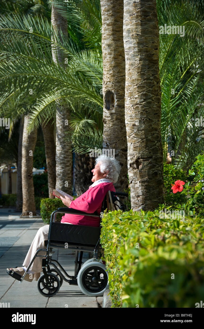 Happy seniors en fauteuil roulant vacances dame détendue senior personnes handicapées lecture d'un livre dans des vacances ensoleillées et sans danger de vacances de palmier de circulation Banque D'Images