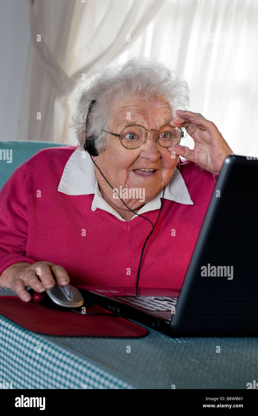 La dame âgée sénior isolant covid-19 porte un casque est étonné par les possibilités de communication sur son écran d'ordinateur portable à la maison Banque D'Images