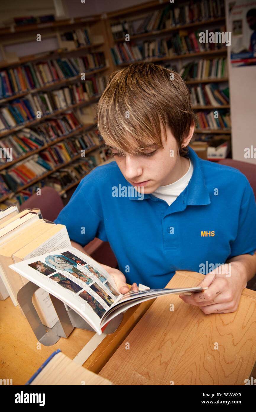 An 8 garçon lisant un livre dans la bibliothèque d'une école secondaire de Galles UK Banque D'Images