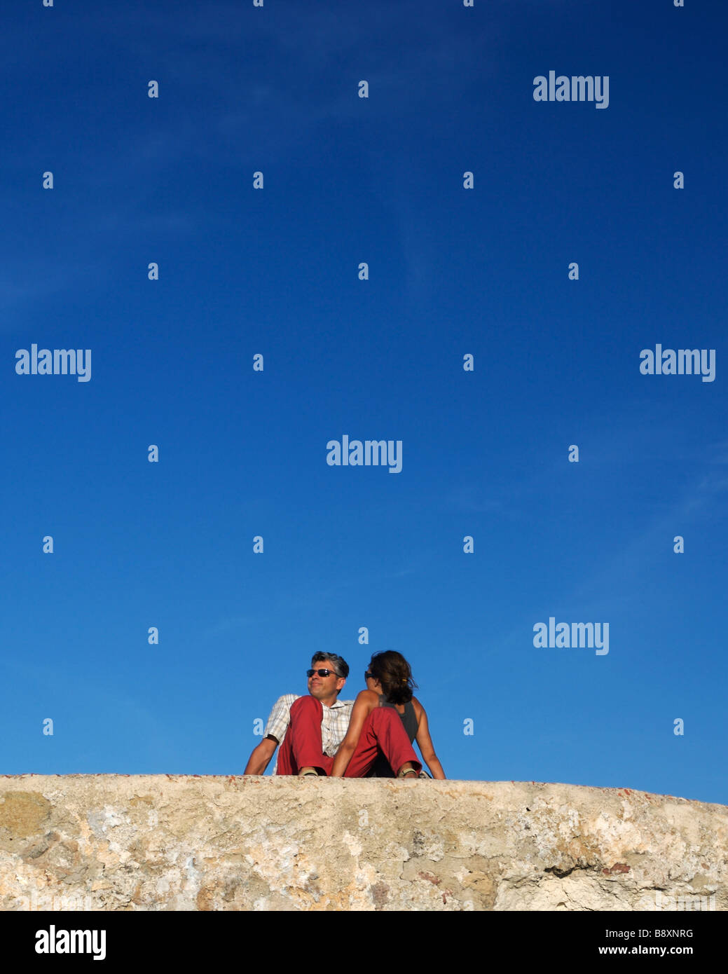 Couple assis sur un mur en pantalon rouge à Alghero, Sardaigne Banque D'Images