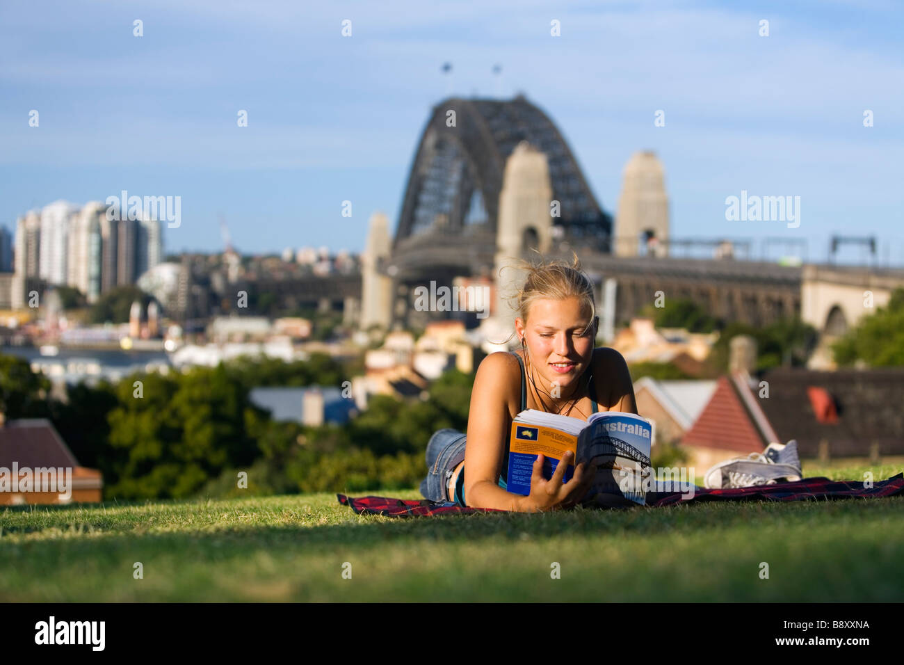 Une jeune femme lit un livre guide sur la colline de l'Observatoire, surplombant le port de Sydney. Sydney, New South Wales, Australia Banque D'Images