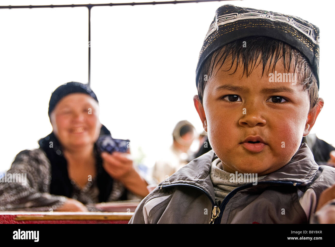 Garçon à la recherche de l'appareil photo avec la femme comme arrière-plan, la vallée de Ferghana, en Ouzbékistan, en Asie Banque D'Images