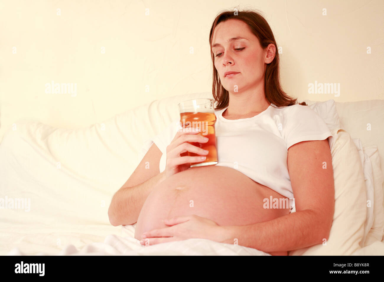 Enceintes fortement déprimé woman holding pint verre de bière blonde de l'alcool sur le dessus de l'alcool au niveau de l'estomac par tapotement exposés accueil Banque D'Images