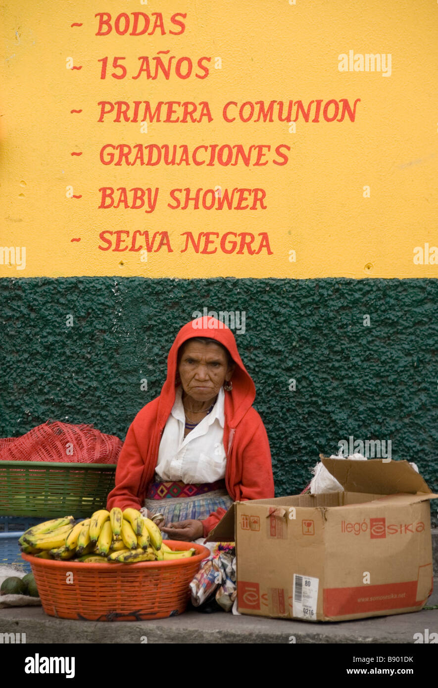 Femme en veste rouge vend des bananes dans le cadre du texte de la publicité d'une boutique de confiseurs. Ipala, au Guatemala. Banque D'Images