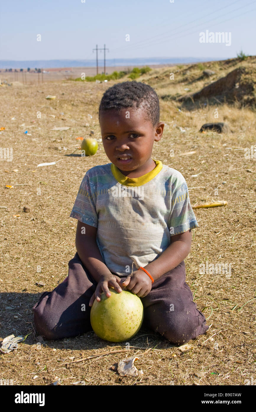 Un enfant s'amuse en jouant avec un melon alors que sa mère travaille dans un décrochage sur le côté de la route au Lesotho Banque D'Images