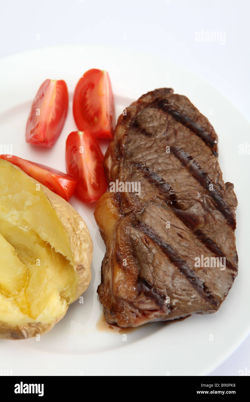 Un faux filet grillé ou New York steak d'aloyau avec pomme de terre au four et de quartiers de tomates fraîches Banque D'Images