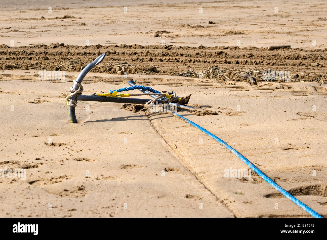 Une ancre repose dans le sable avec une corde bleu attatched Banque D'Images