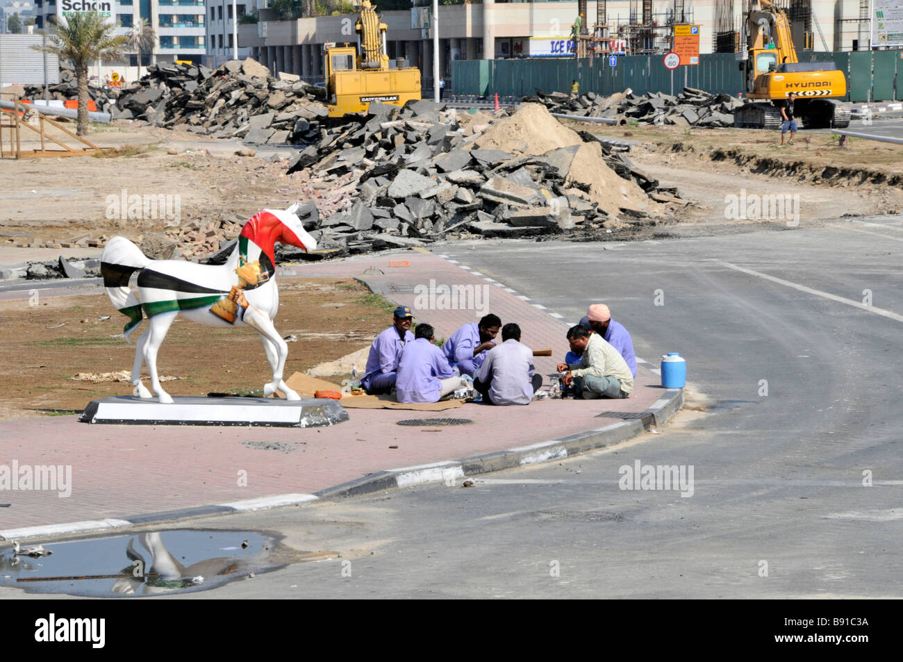 Scène de rue de Dubaï à l'industrie de construction de bâtiment groupe de site de Pause repas des travailleurs assis sur le trottoir avec statue de cheval unie Émirats arabes Unis Banque D'Images