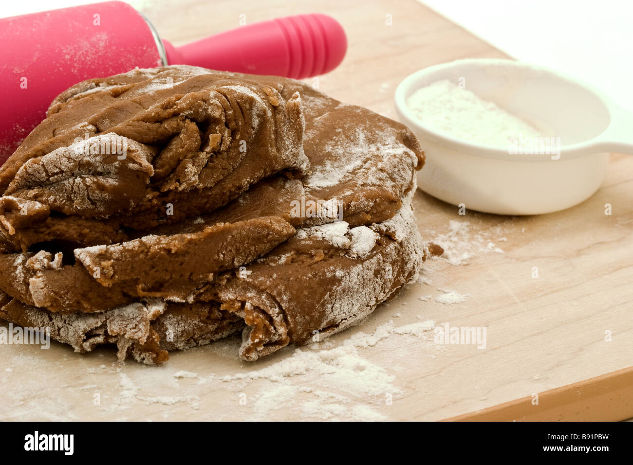Rouleau à pâte rose et gingerbread cookie pâte sur une planche à découper en bois et une petite tasse de mesure de farine Banque D'Images
