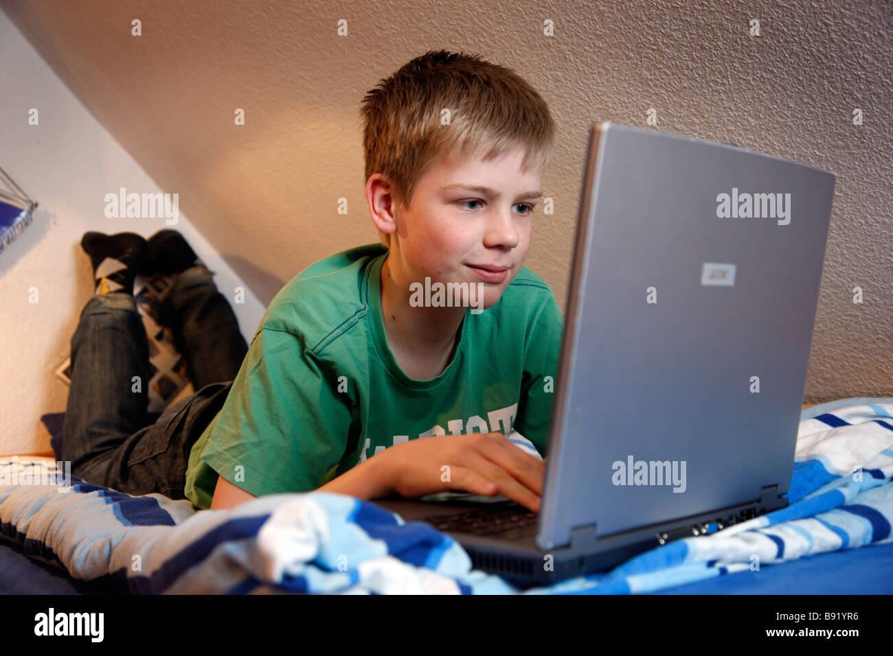 Un garçon, 13 ans, travaille à son ordinateur portable posé sur son lit  dans sa chambre de l'enfant Photo Stock - Alamy