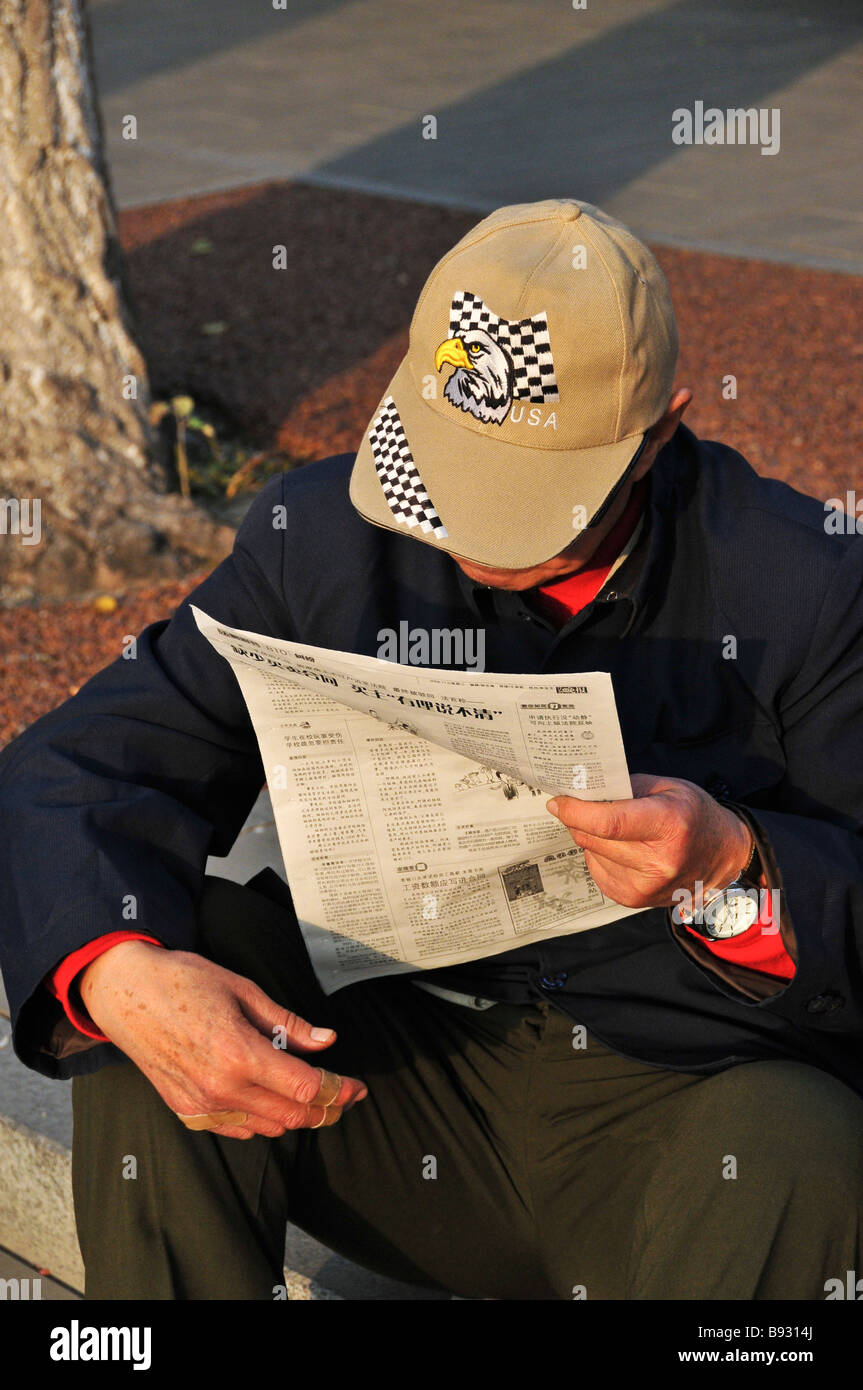 Chinese man reading newspaper portant une casquette à Beijing Chine Banque D'Images