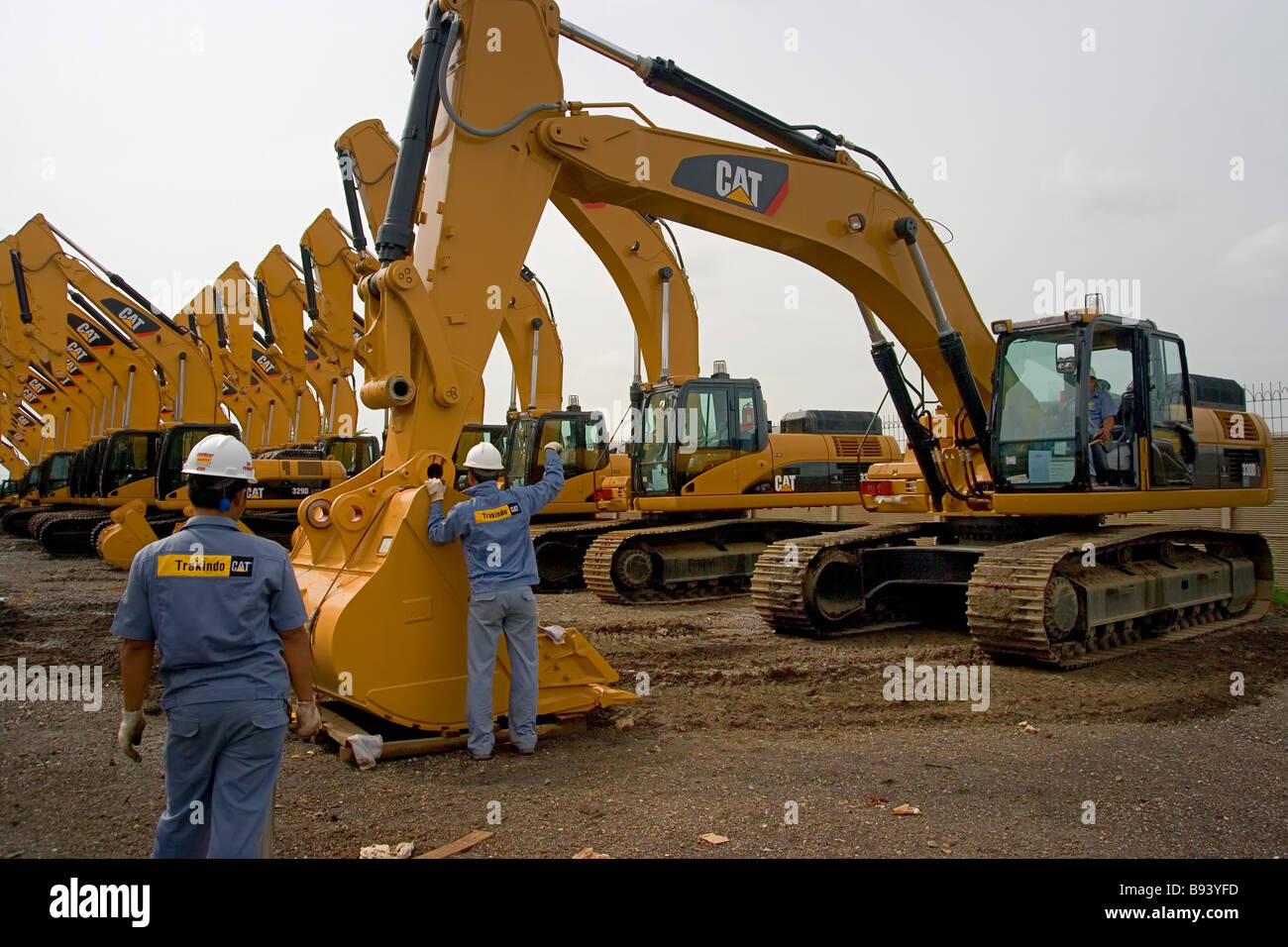 Deux ingénieurs travaillent sur l'excavatrice caterpillar pour installer le godet, stationné dans le stockage extérieur ouvert en répétition Banque D'Images