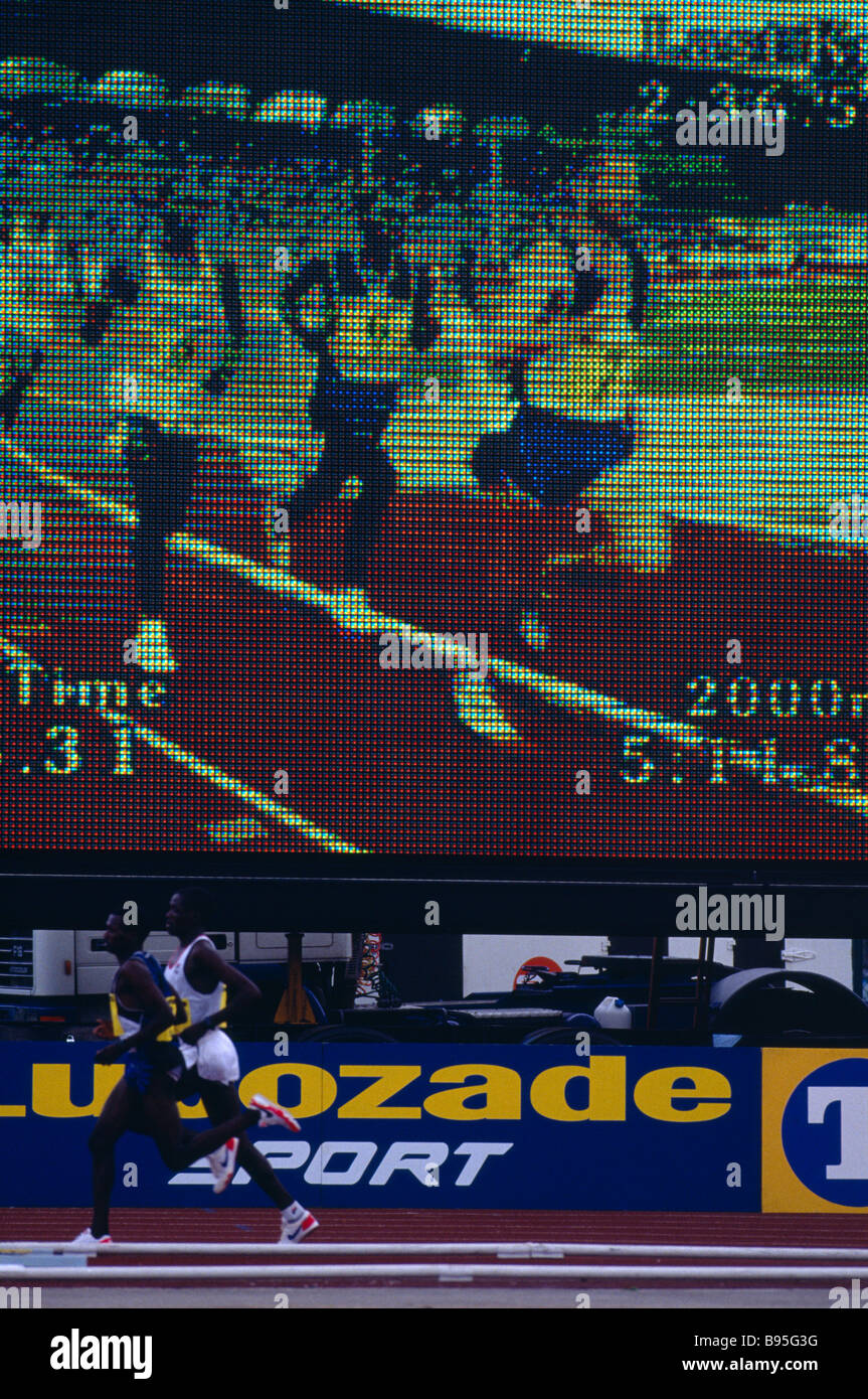 Sportifs Athlétisme athlètes masculins en cours lors d'une réunion en cours d'exécution au-delà d'un écran de consultation électronique Banque D'Images