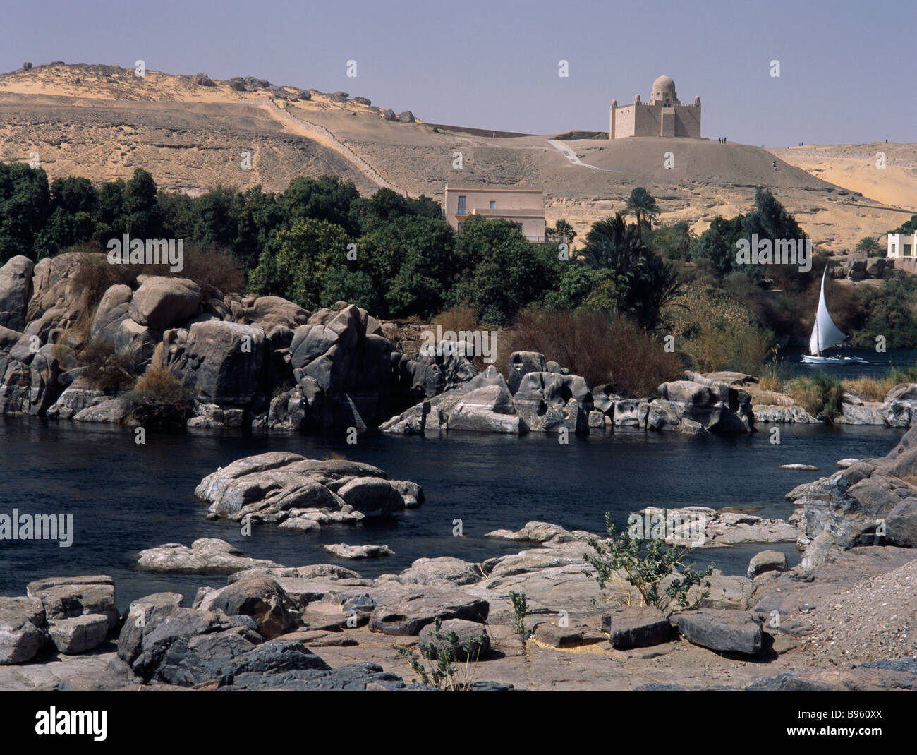 Égypte, vallée du Nil, Assouan. Felouque sur le Nil au premier plan avec le mausolée de l'Aga Khan sur colline au-delà. Banque D'Images