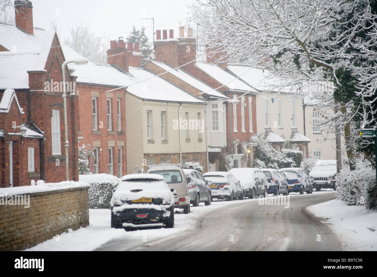 Voitures garées à l'extérieur des maisons sur une route enneigée dans un village d'Angleterre en hiver. Banque D'Images