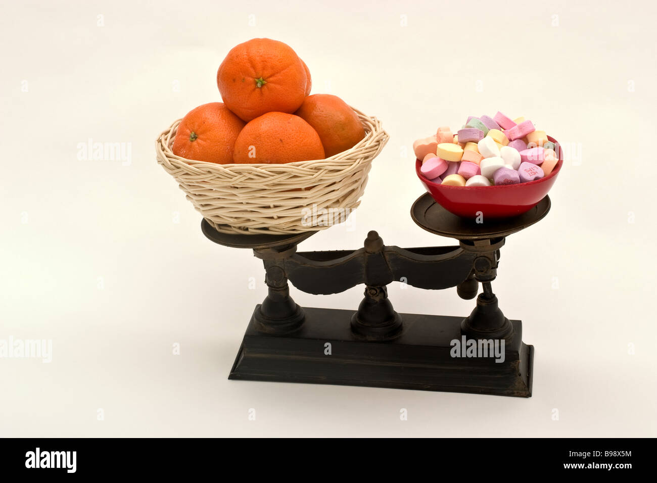 Balance avec un panier d'oranges sur un côté et une bonbonnière remplis de  bonbons de l'autre Photo Stock - Alamy