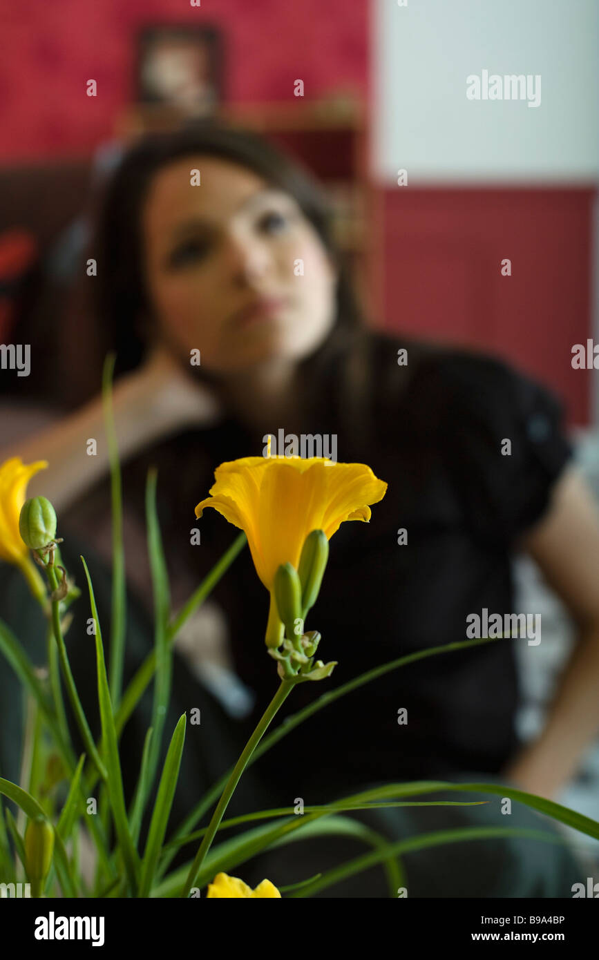 Femme assise, holding head, se concentrer sur des plantes à fleurs en premier plan Banque D'Images