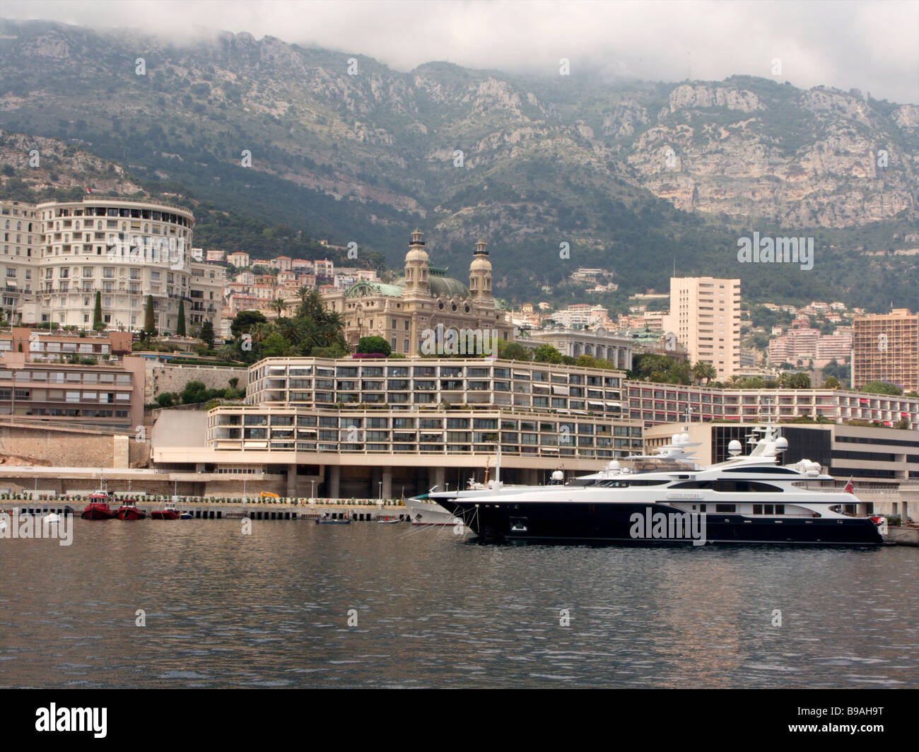 Un yacht de luxe amarrés dans le port port de Monaco Monte Carlo dans l'ombre des montagnes de nuages bas Banque D'Images