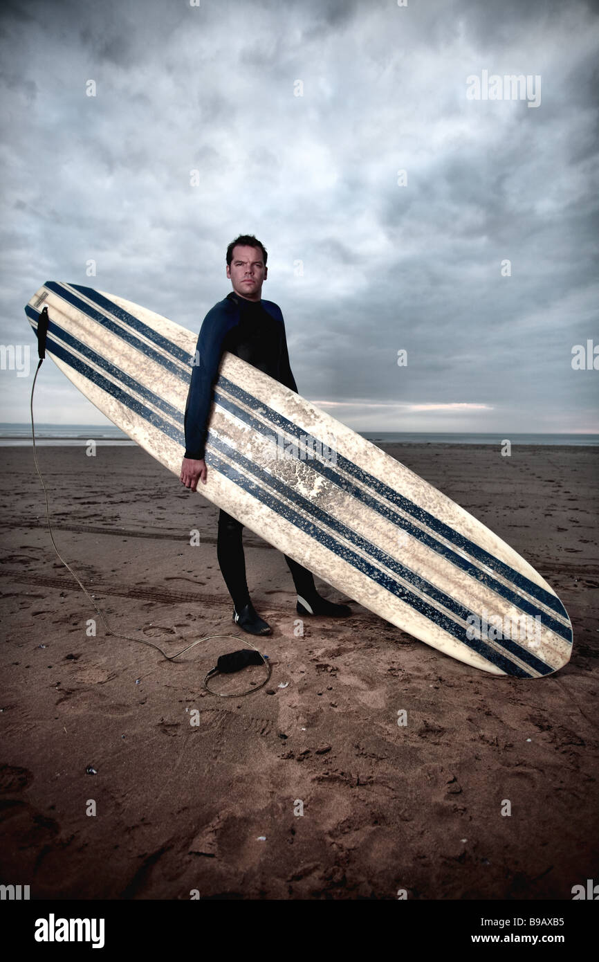 Surfer mâle avec de long board se dresse sur la plage Devon Banque D'Images