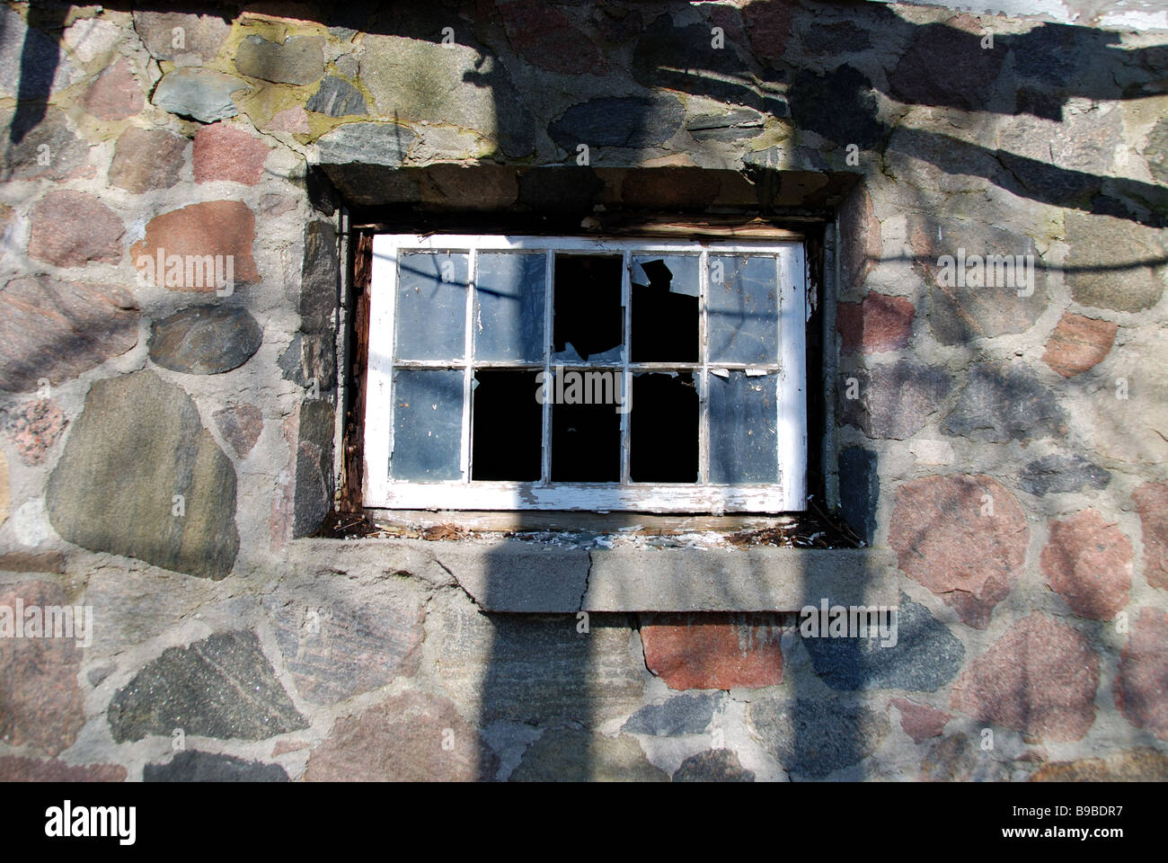 Le côté d'une vieille maison en pierre avec brisé des fenêtres dans le besoin de réparation. Banque D'Images