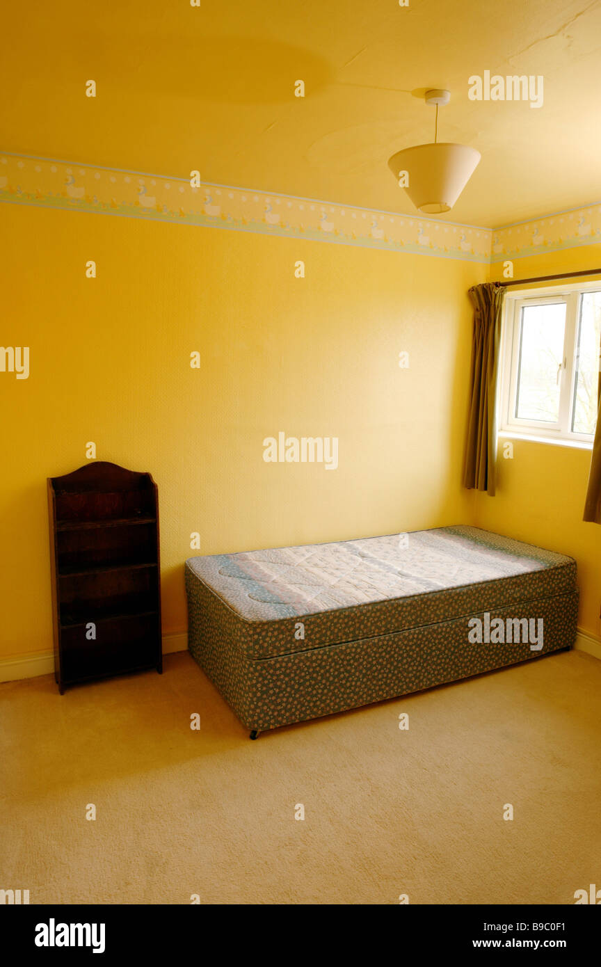 Une chambre vide avec des murs jaunes et un lit vide dans le coin sous une  fenêtre avec des rideaux de style ancien Photo Stock - Alamy