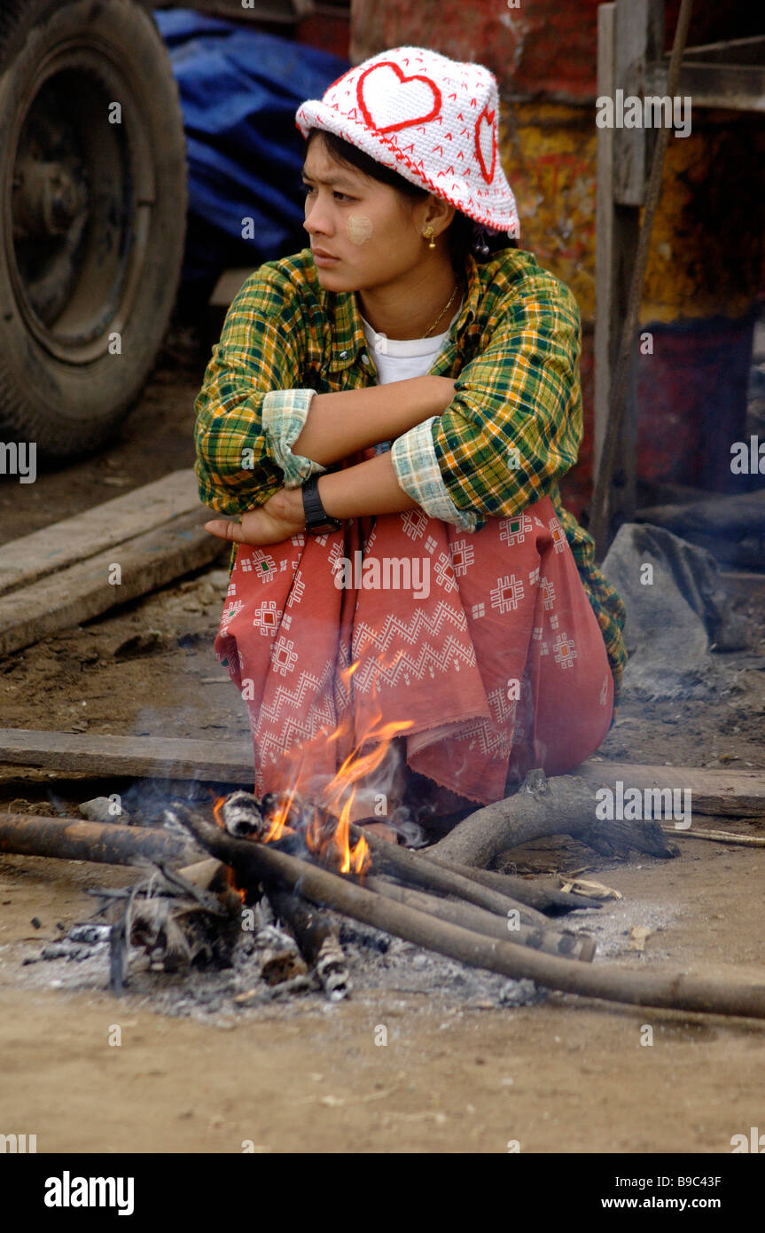 Birmese femme assis sur un petit feu par une froide matinée au port de ferries de Mandalay Myanmar Banque D'Images