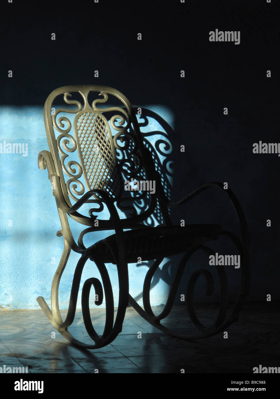 Un fauteuil à bascule en métal, en partie dans l'ombre, contre un mur bleu Banque D'Images