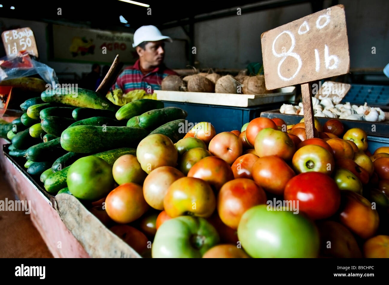 Tomates et concombres juteux à la vente à un marché alimentaire intérieur à Cuba avec le vendeur dans l'arrière-plan. Banque D'Images