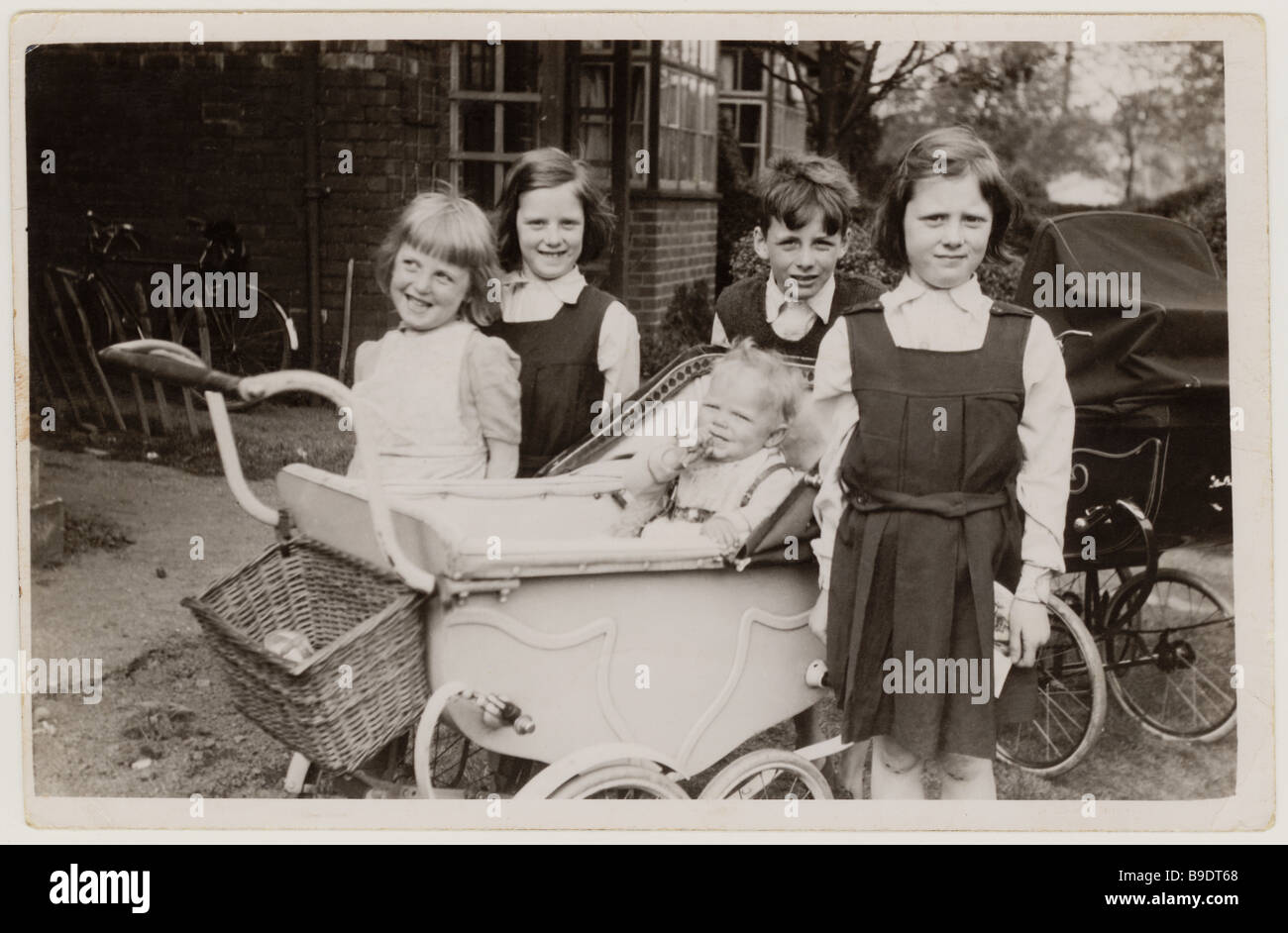 Photo originale effrontée jeunes écoliers des années 1950 avec des landaus s'occupant d'un bébé à l'extérieur de leur maison familiale dans les années 1950, Royaume-Uni Banque D'Images