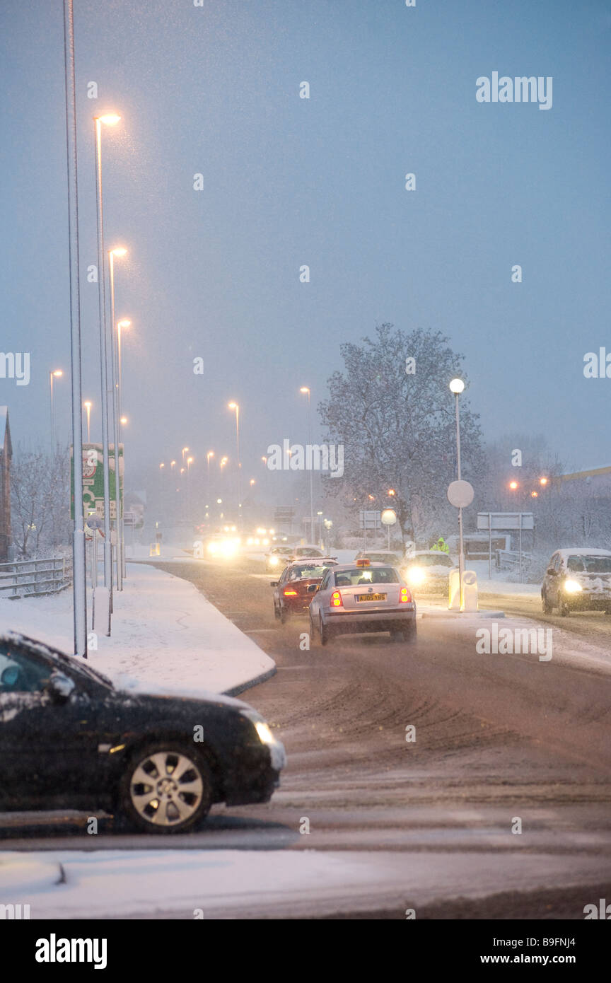 Les voitures qui circulent le long d'une route couverte de neige sur une soirée hivers en Angleterre Banque D'Images