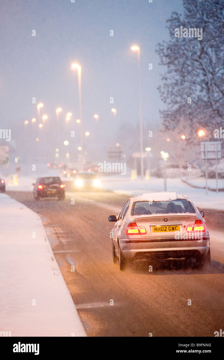 Les voitures qui circulent le long d'une route couverte de neige sur une soirée hivers en Angleterre Banque D'Images