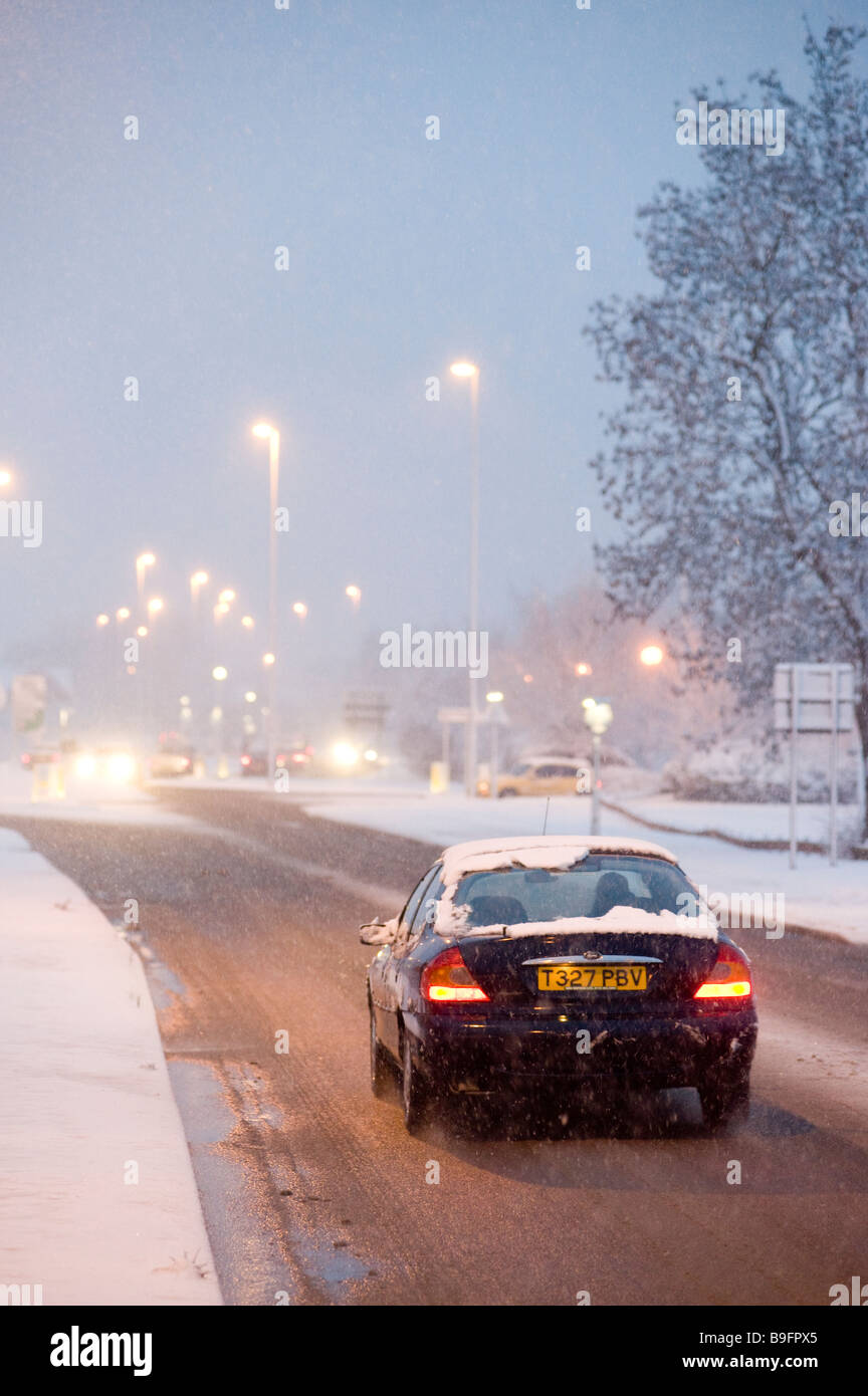 Les voitures qui circulent le long d'une route couverte de neige sur une soirée hivers en Angleterre Banque D'Images